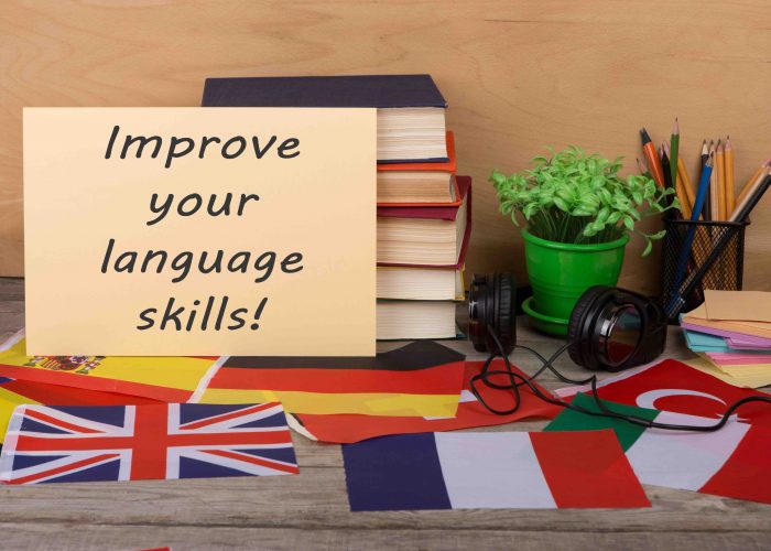 Learning languages concept - paper with text "Improve your language skills!", flags, books, headphones, pencils on wooden background